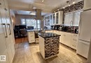Kitchen featuring tile flooring, white cabinetry with contemporary hardware, black countertops, and a full-height mosaic tile backsplash - 6704 93 Street, Edmonton, AB 