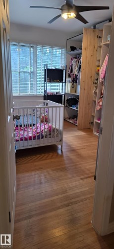 Wood-finish flooring throughout, featuring a window with horizontal blinds and a ceiling fan with integrated lighting - 6704 93 Street, Edmonton, AB 