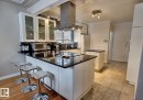 Modern kitchen featuring a breakfast bar with seating, white shaker-style cabinetry, dark countertops, and stainless steel appliances - 6704 93 Street, Edmonton, AB 