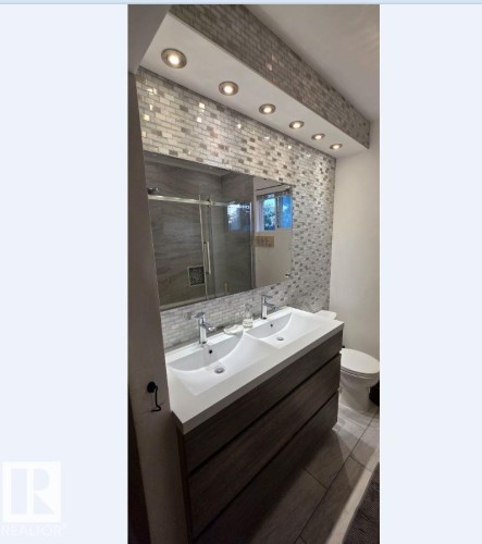 Modern bathroom featuring a dual vanity with integrated sinks, chrome fixtures, and wood-finish cabinetry - 6704 93 Street, Edmonton, AB 