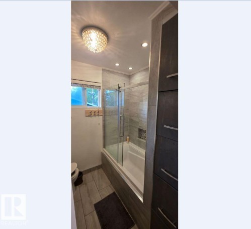 Bathroom featuring a tiled tub-shower combination with glass enclosure, recessed shower niche, and dark wood-finish cabinetry - 6704 93 Street, Edmonton, AB 