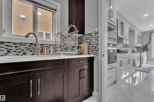 Modern kitchen featuring a mosaic tile backsplash, stainless steel appliances, dark wood-finish cabinetry, and light-tone flooring - 2419 15 Avenue, Edmonton, AB 