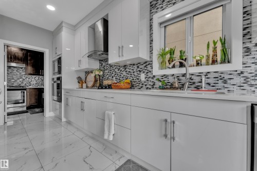 Contemporary kitchen featuring glossy white cabinetry, stainless steel appliances, a mosaic tile backsplash, and a large window above the sink - 2419 15 Avenue, Edmonton, AB 