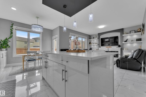 Open-concept living space featuring a central island with a solid surface countertop, white high-gloss cabinetry with bar pulls, large format tile flooring, and recessed lighting - 2419 15 Avenue, Edmonton, AB 