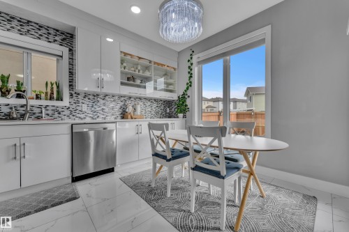 Modern kitchen featuring a mosaic tile backsplash, stainless steel dishwasher, white flat-panel cabinetry, and white marble-look tile flooring - 2419 15 Avenue, Edmonton, AB 