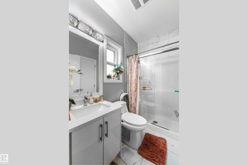 Bathroom featuring a white vanity with integrated sink, a frameless mirror, a sliding glass shower enclosure, and white marble-look wall tiling - 2419 15 Avenue, Edmonton, AB 