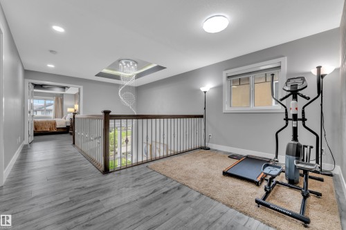 Open loft area featuring wood-finish flooring, a contemporary chandelier within a recessed ceiling, and a wood and metal staircase railing - 2419 15 Avenue, Edmonton, AB 