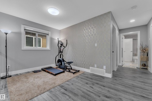 Versatile interior space featuring wood-finish flooring, a window with white trim, and a wall with a geometric patterned accent - 2419 15 Avenue, Edmonton, AB 