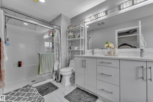 Contemporary bathroom featuring a dual vanity with a light countertop and undermount sinks, a spacious mirror, and overhead vanity lighting - 2419 15 Avenue, Edmonton, AB 