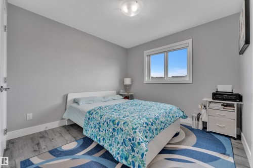 Bedroom featuring a window with white trim, light gray painted walls, and wood-finish flooring - 2419 15 Avenue, Edmonton, AB 