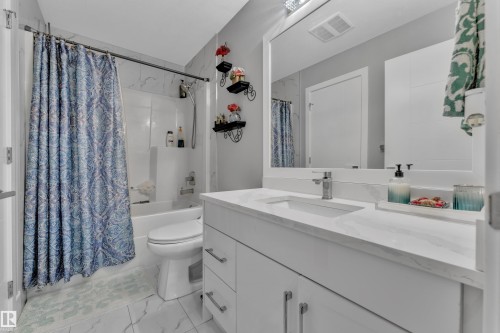 Contemporary bathroom featuring a white vanity with an integrated sink, a large framed mirror, and a combination tub/shower with a tiled surround - 2419 15 Avenue, Edmonton, AB 