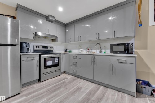 Kitchen featuring light grey cabinetry, stainless steel appliances, a tile backsplash, and light wood-finish flooring - 2419 15 Avenue, Edmonton, AB 