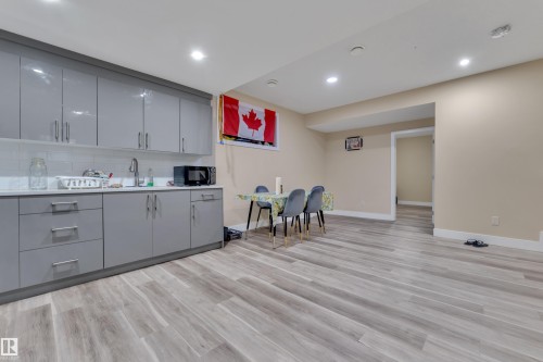 Open-concept space featuring wood-finish flooring, recessed lighting, and a kitchen area with gray cabinetry, white subway tile backsplash, and a white countertop - 2419 15 Avenue, Edmonton, AB 