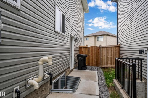 Exterior siding in a neutral gray tone with a basement window well, a light-colored entry door, and a concrete walkway - 2419 15 Avenue, Edmonton, AB 