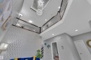 Two-story interior with a tiered crystal chandelier, upper-level landing with dark wood railing and metal spindles, recessed lighting, and a textured accent wall - 2419 15 Avenue, Edmonton, AB 