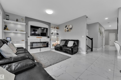 Living area featuring a contemporary electric fireplace with a marble-finish surround, built-in shelving with integrated lighting, and large format marble-finish floor tiles - 2419 15 Avenue, Edmonton, AB 