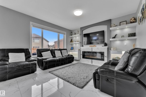 Contemporary living space featuring large format tile flooring, a prominent decorative fireplace with a glass front, and built-in shelving with integrated lighting - 2419 15 Avenue, Edmonton, AB 