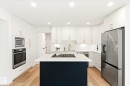 Kitchen featuring a dark-toned island with an integrated cooktop, white perimeter cabinetry, stainless steel appliances, and wood-finish flooring - 5716 175 Street, Edmonton, AB 