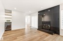 Spacious living area featuring a sleek, dark tile fireplace with a hearth, recessed lighting, wood-finish flooring, and a built-in bar area with open shelving and a beverage refrigerator - 5716 175 Street, Edmonton, AB 