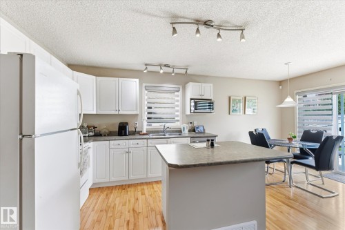 Kitchen with wood-finish flooring, white cabinetry, track lighting, and a kitchen island - 37 4020 21 Street, Edmonton, AB 