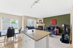 Open-concept living space featuring wood-finish flooring, a kitchen island with storage, a dining area with a glass patio door, a living room with carpet flooring, and a fireplace with a mantel - 