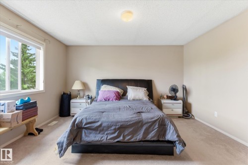 Carpeted bedroom featuring a large window, neutral wall paint, a flush-mount ceiling light, and white baseboards - 37 4020 21 Street, Edmonton, AB 
