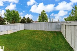 Expansive yard featuring a manicured lawn, full perimeter privacy fencing, and mature trees beyond - 