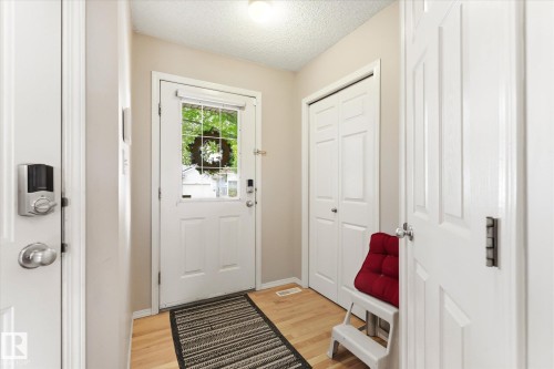 Entryway featuring light wood-finish flooring, a white front door with an integrated glass panel, a smart lock system, and bi-fold closet doors - 37 4020 21 Street, Edmonton, AB 
