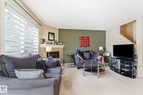 Living area featuring a textured accent wall, light-colored carpeting, and a fireplace with a stone surround and mantel - 37 4020 21 Street, Edmonton, AB 