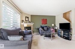 Living area featuring a textured accent wall, light-colored carpeting, and a fireplace with a stone surround and mantel - 