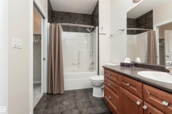 Bathroom featuring a wood-finish vanity with an integrated sink, dark countertop, and large mirror - 