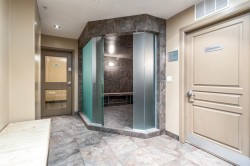 Sauna room featuring frosted glass entrance, tile flooring, built-in wooden bench seating, and wall-mounted lighting - 