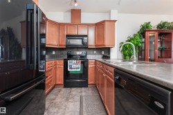 U-shaped kitchen featuring wood cabinetry, dark countertops, black appliances, a double basin sink with a high-arc faucet, and tiled flooring - 