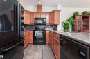 U-shaped kitchen featuring wood cabinetry, dark countertops, black appliances, a double basin sink with a high-arc faucet, and tiled flooring - 439 300 Palisades Way, Sherwood Park, AB  - Indoor Photo Showing Kitchen With Double Sink 