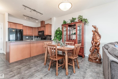 Open-concept kitchen and dining area featuring wood-finish cabinetry, black appliances, track lighting, and tile flooring - 439 300 Palisades Way, Sherwood Park, AB - Indoor