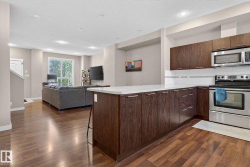 Modern kitchen featuring dark wood cabinetry, white countertops, stainless steel appliances, and a white subway tile backsplash - 30 6075 Schonsee Way, Edmonton, AB 