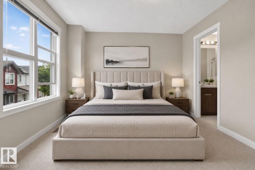 Spacious bedroom featuring light neutral wall tones, plush carpet flooring, large multi-pane windows, and a doorway opening to an en-suite bathroom with a dark wood-finish vanity - 30 6075 Schonsee Way, Edmonton, AB 