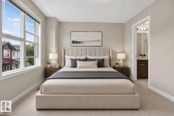 Spacious bedroom featuring light neutral wall tones, plush carpet flooring, large multi-pane windows, and a doorway opening to an en-suite bathroom with a dark wood-finish vanity - 