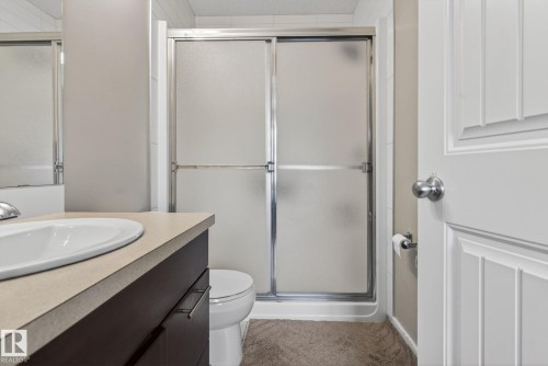 Bathroom featuring a sliding glass shower enclosure, a dark wood-finish vanity with an integrated basin, a light-toned countertop, and a white paneled door with chrome hardware - 30 6075 Schonsee Way, Edmonton, AB 