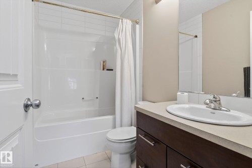 Bathroom featuring a white tub and shower combination with tile surround, a dark wood-finish vanity with a light countertop, a white oval undermount sink, and a chrome faucet - 30 6075 Schonsee Way, Edmonton, AB 