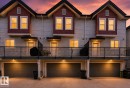 Multi-level townhouse exterior featuring light-toned horizontal siding, red shake accents, and dark pitched roofs - 30 6075 Schonsee Way, Edmonton, AB 