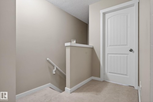 Carpeted landing featuring a white paneled door with a brushed nickel knob, neutral wall paint, and white trim - 30 6075 Schonsee Way, Edmonton, AB 