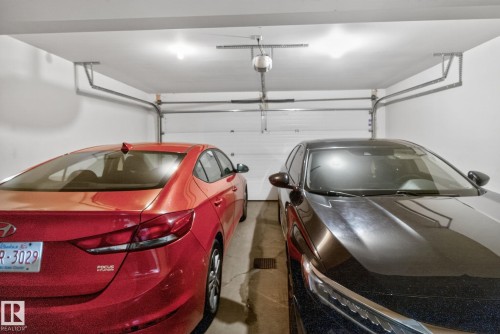 Two-car garage featuring white painted walls and ceiling, two overhead light fixtures, and a white paneled garage door - 30 6075 Schonsee Way, Edmonton, AB 