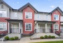 Townhouse exterior featuring red and gray siding, black gables, white trim windows, covered entryways with columns, and black metal railings - 30 6075 Schonsee Way, Edmonton, AB 