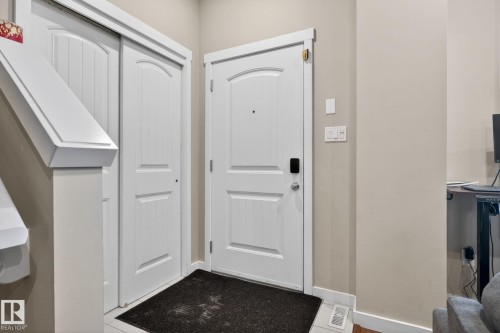 Entryway featuring a white paneled door with smart lock hardware, a white two-panel sliding closet door, and light neutral wall paint - 30 6075 Schonsee Way, Edmonton, AB 