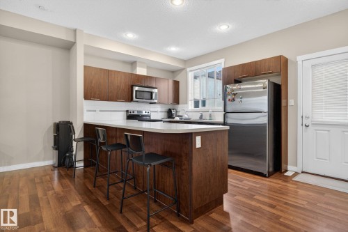 Kitchen featuring wood-finish flooring, an island with countertop seating, stainless steel appliances, white subway tile backsplash, and recessed lighting - 30 6075 Schonsee Way, Edmonton, AB 
