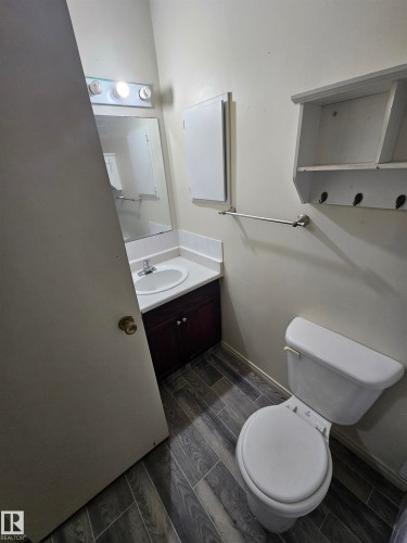 Bathroom featuring wood-finish flooring, a white vanity with an integrated sink, a wall-mounted medicine cabinet, and a white toilet - 401 10615 110 Street, Edmonton, AB 
