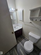Bathroom featuring wood-finish flooring, a white vanity with an integrated sink, a wall-mounted medicine cabinet, and a white toilet - 