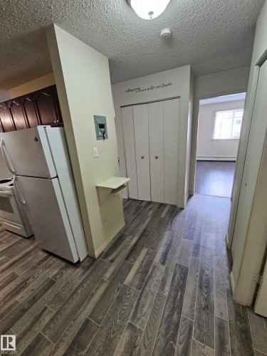Wood-finish plank flooring extends through the hallway, complemented by a recessed ceiling light fixture - 401 10615 110 Street, Edmonton, AB 