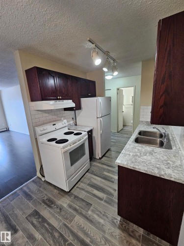 Kitchen featuring wood-finish cabinetry, a white appliance package, and wood-finish flooring - 401 10615 110 Street, Edmonton, AB 